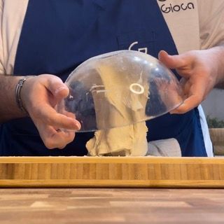 Un uomo che indossa un grembiule blu tiene una ciotola trasparente su un tagliere di legno