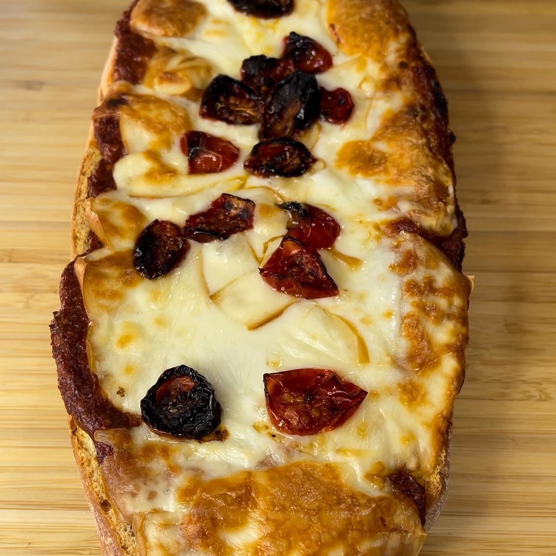 Primo piano di una pizza con formaggio e pomodori su un tavolo di legno.
