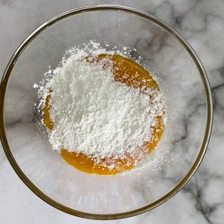 Una ciotola di vetro piena di zucchero a velo e un liquido giallo