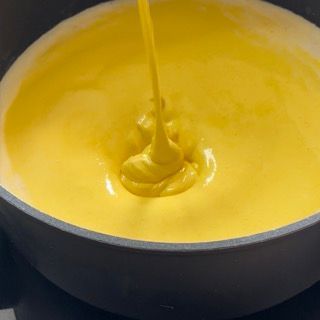 Primo piano di una ciotola di salsa gialla versata in una padella.