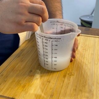 Una persona sta mescolando qualcosa in una tazza graduata con un cucchiaio