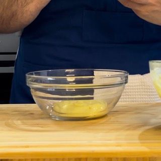 Una ciotola di vetro piena di liquido giallo è appoggiata su un tavolo di legno