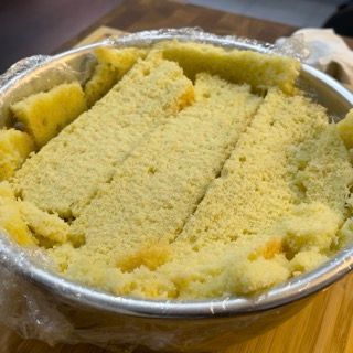 Una ciotola di metallo piena di una torta gialla appoggiata su un tavolo di legno.