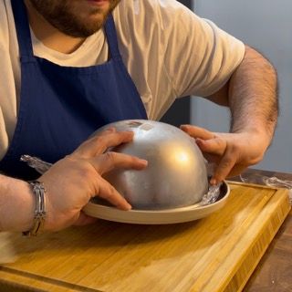 Un uomo con un grembiule tiene in mano una cupola di metallo su un piatto