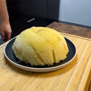 Una grande torta gialla su un piatto nero su un tagliere di legno