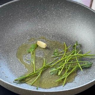 Aglio e gambi di prezzemolo che soffriggono in una padella capiente con olio EVO.
