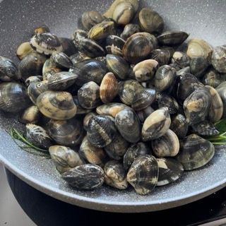 Vongole che si aprono in padella con il coperchio durante la cottura.
