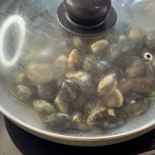 Vongole che si aprono in padella con il coperchio durante la cottura.