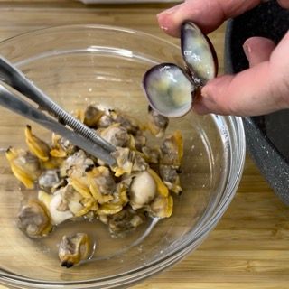 Mano che sguscia con pazienza le vongole cotte in una ciotolina.