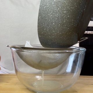 Liquido di cottura delle vongole versato in un colino a maglie fini.