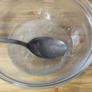 Un cucchiaio è in una ciotola di vetro piena di liquido su un tavolo di legno.