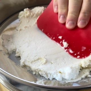 Una persona sta setacciando la farina con una spatola rossa.