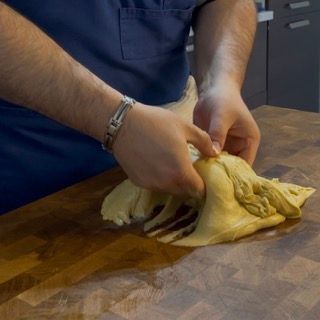 Una persona tiene in mano un pezzo di pasta su un tagliere