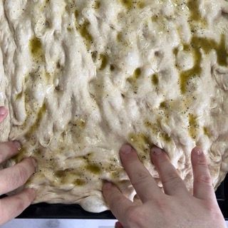 Una persona tiene in mano un pezzo di impasto per pizza.