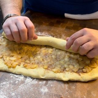 Mani che iniziano ad arrotolare l'impasto farcito dal lato lungo.