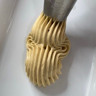 Primo piano di una sac à poche piena di glassa su una superficie bianca.