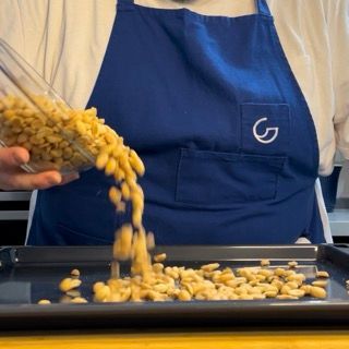 Una persona con un grembiule blu che versa i maccheroni in una padella