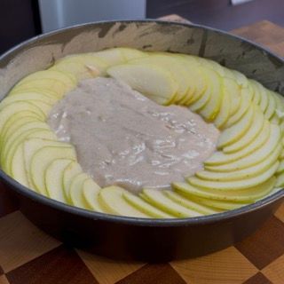 Mani che dispongono con cura le fettine di mela a cerchio sulla superficie della torta.
