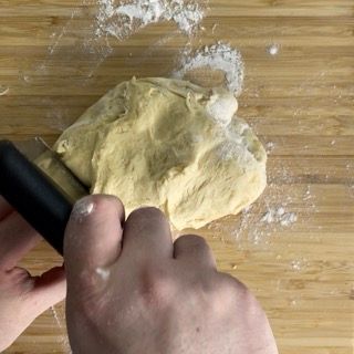 Una persona sta impastando l'impasto su un tagliere di legno.