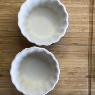 Due ciotole bianche sono appoggiate su un tagliere di legno.