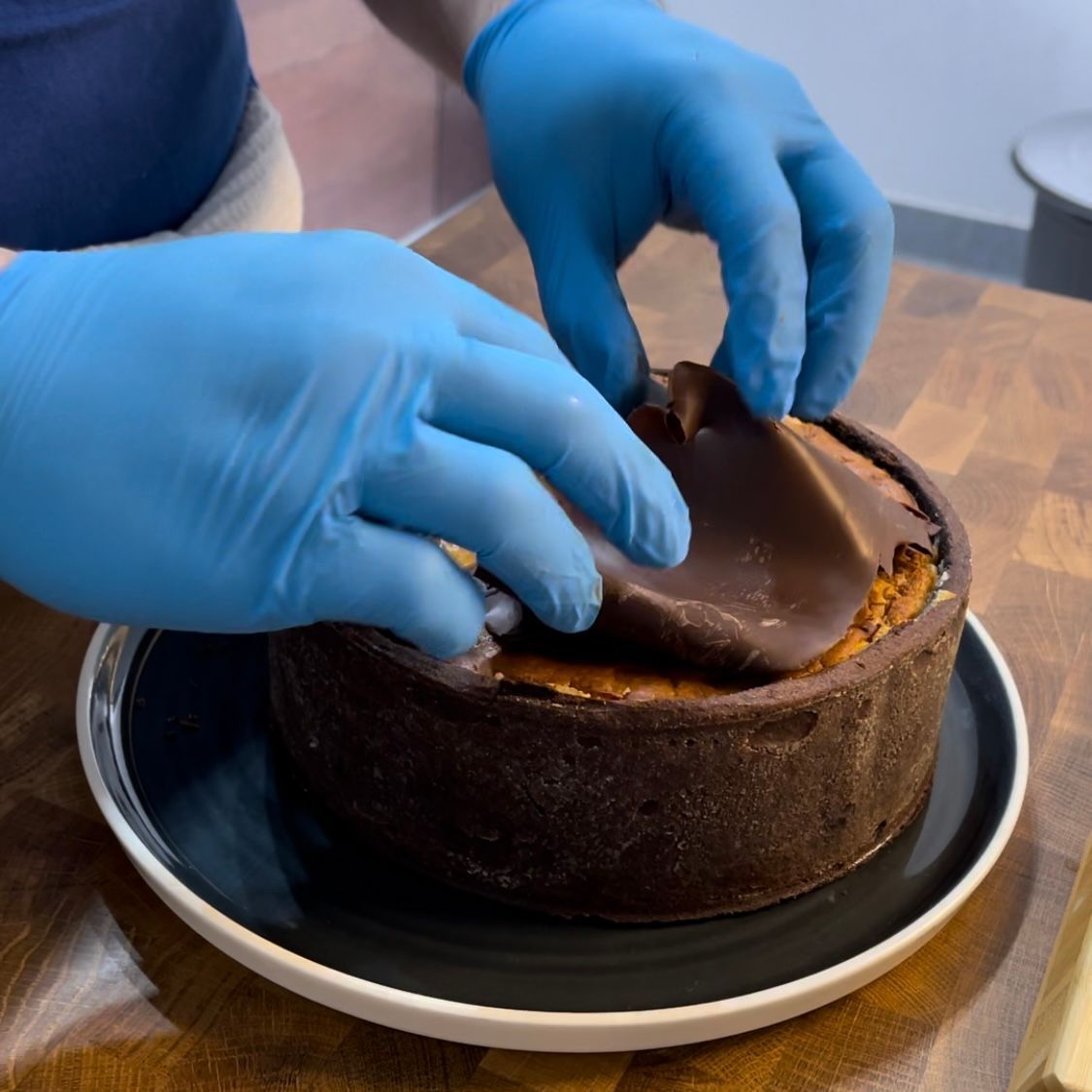 Una persona che indossa guanti blu sta ricoprendo una torta di cioccolato