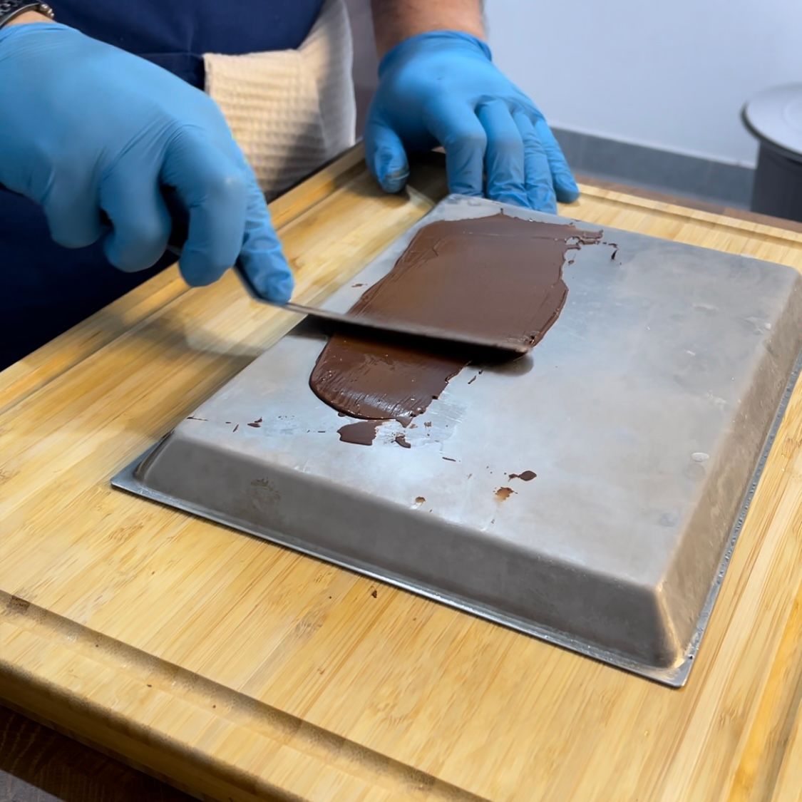 Una persona che indossa guanti blu sta tagliando il cioccolato su un tagliere