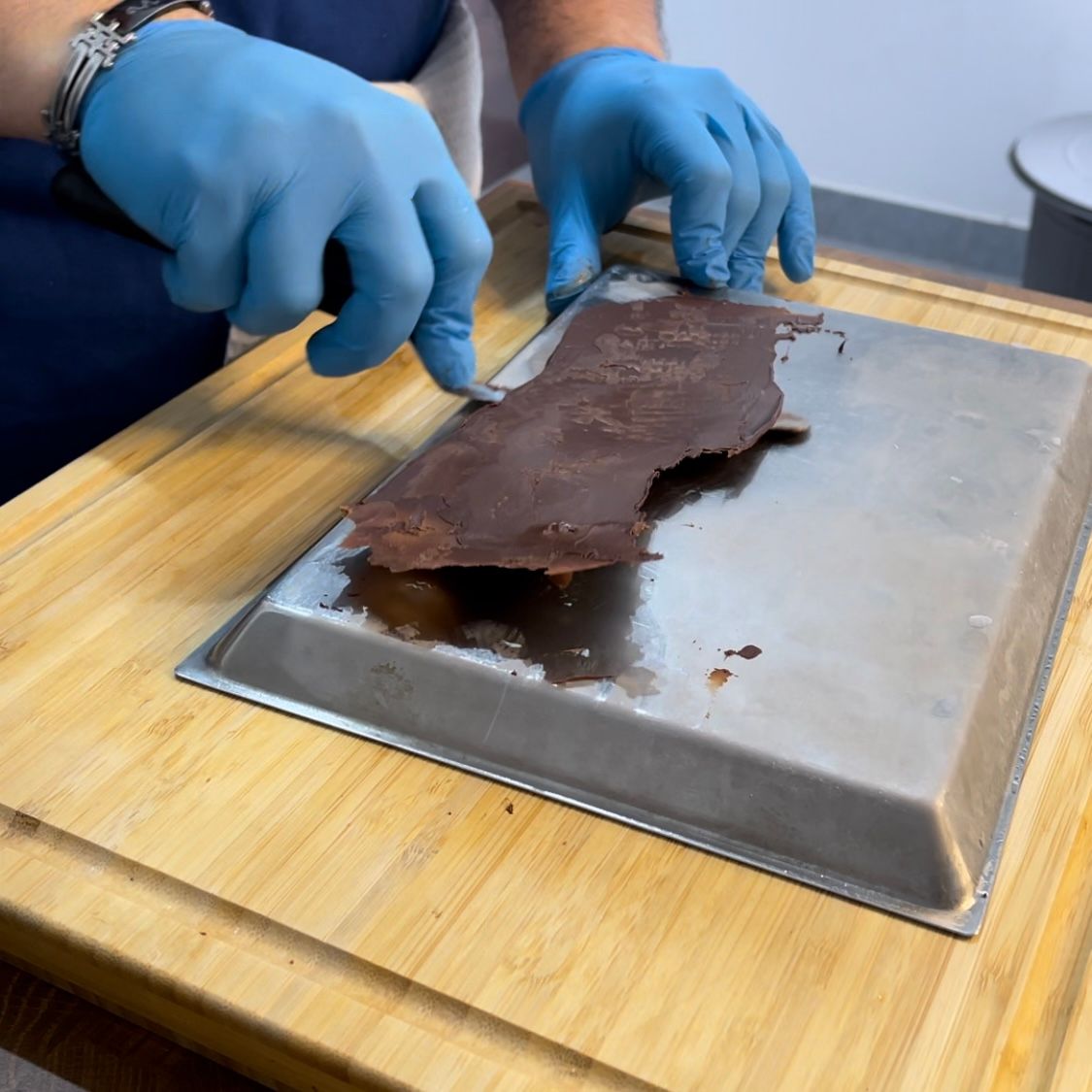 Una persona che indossa guanti blu sta tagliando un pezzo di cioccolato su un vassoio
