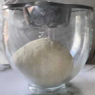 Una ciotola di vetro piena di impasto è appoggiata su un tavolo.