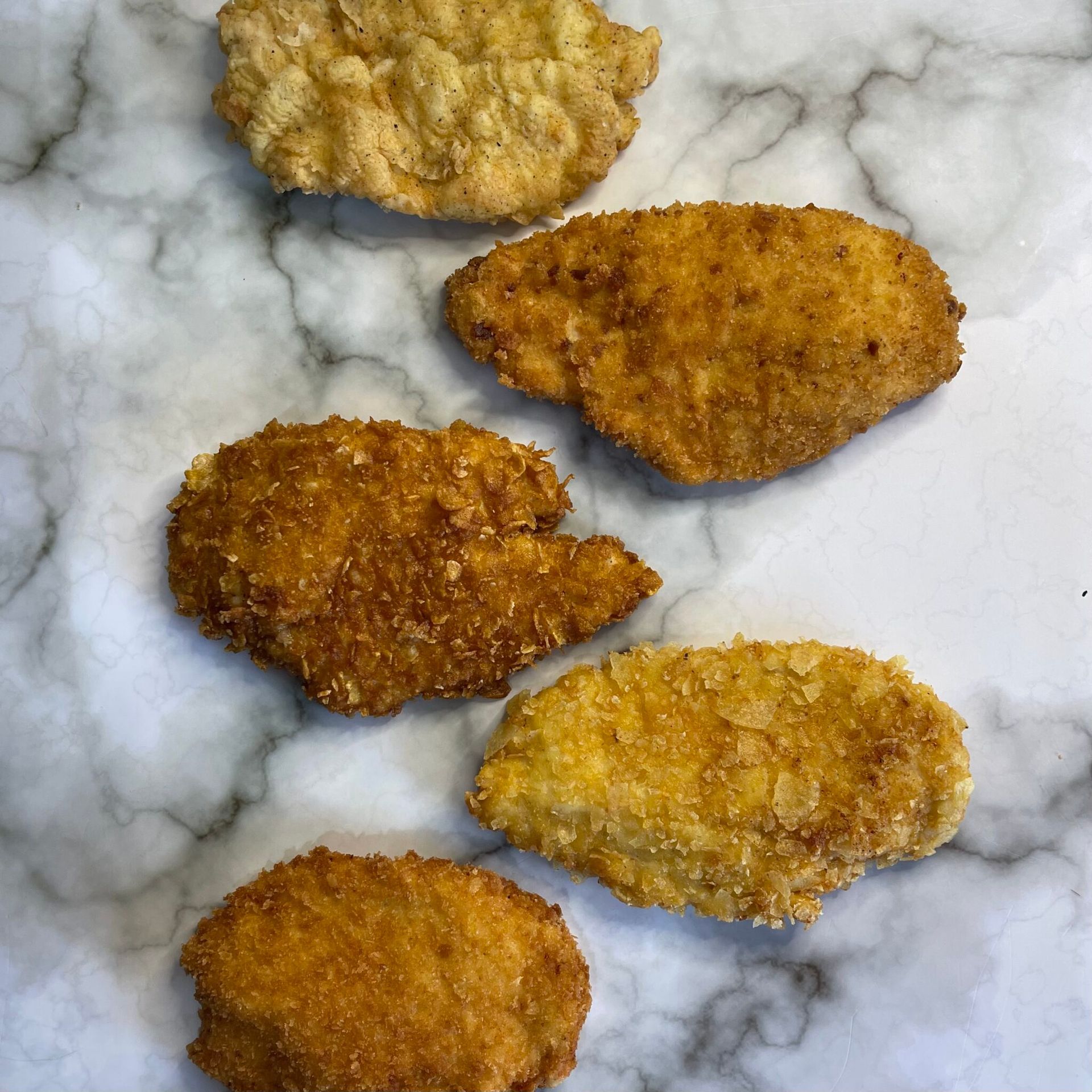 Una fila di bocconcini di pollo fritti su una superficie di marmo.