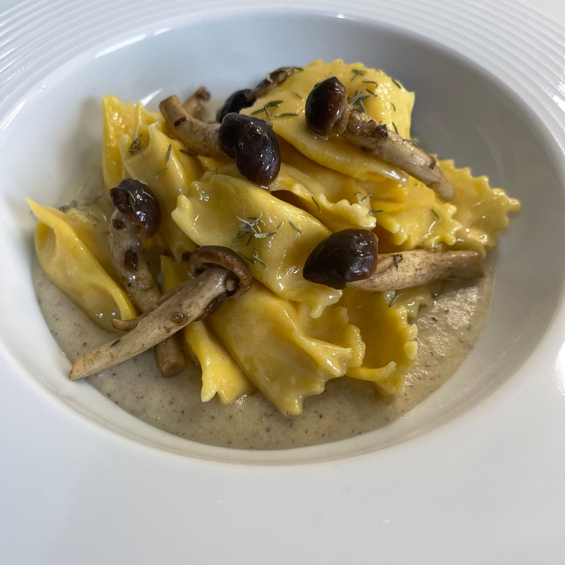 Un piatto bianco con sopra pasta e funghi su un tavolo.