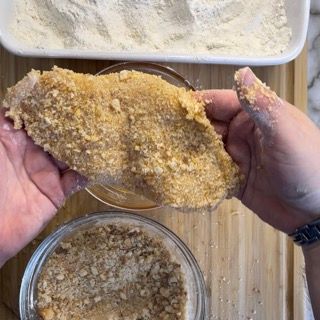 Una persona tiene in mano un pezzo di pollo impanato.