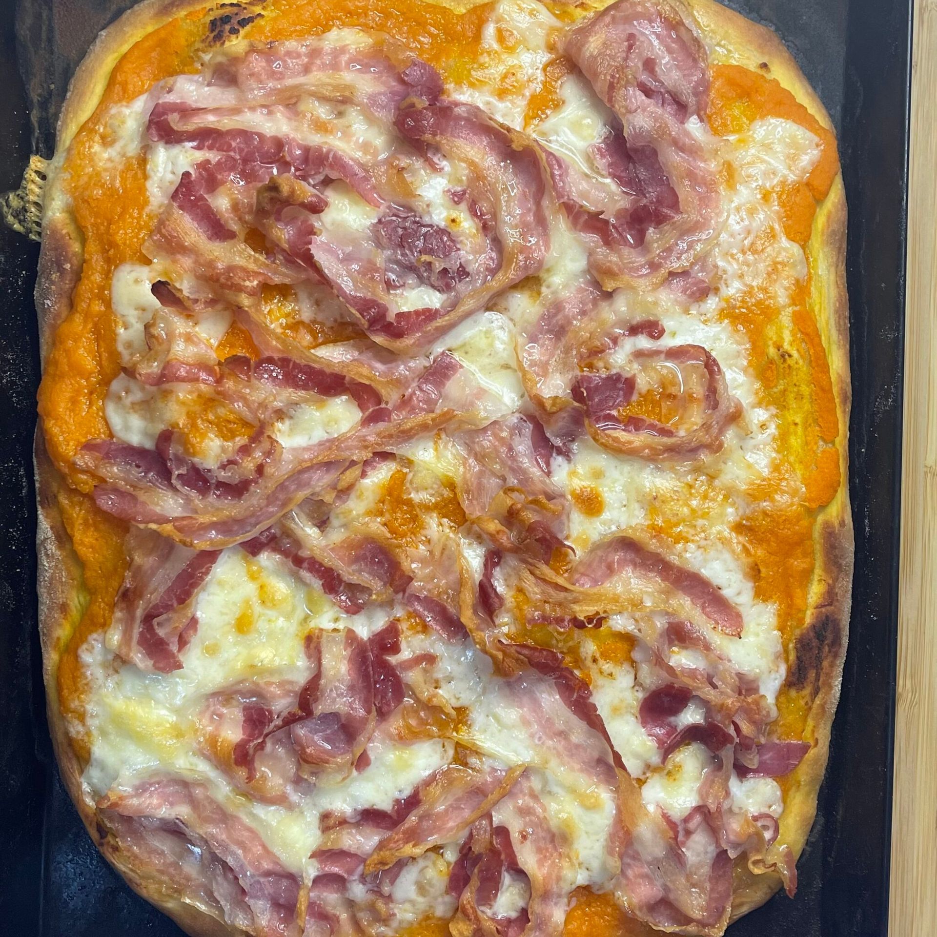 Una pizza con pancetta e formaggio è appoggiata su un tavolo.