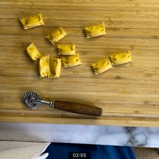 Un tagliere di legno con sopra i ravioli e un tagliapasta