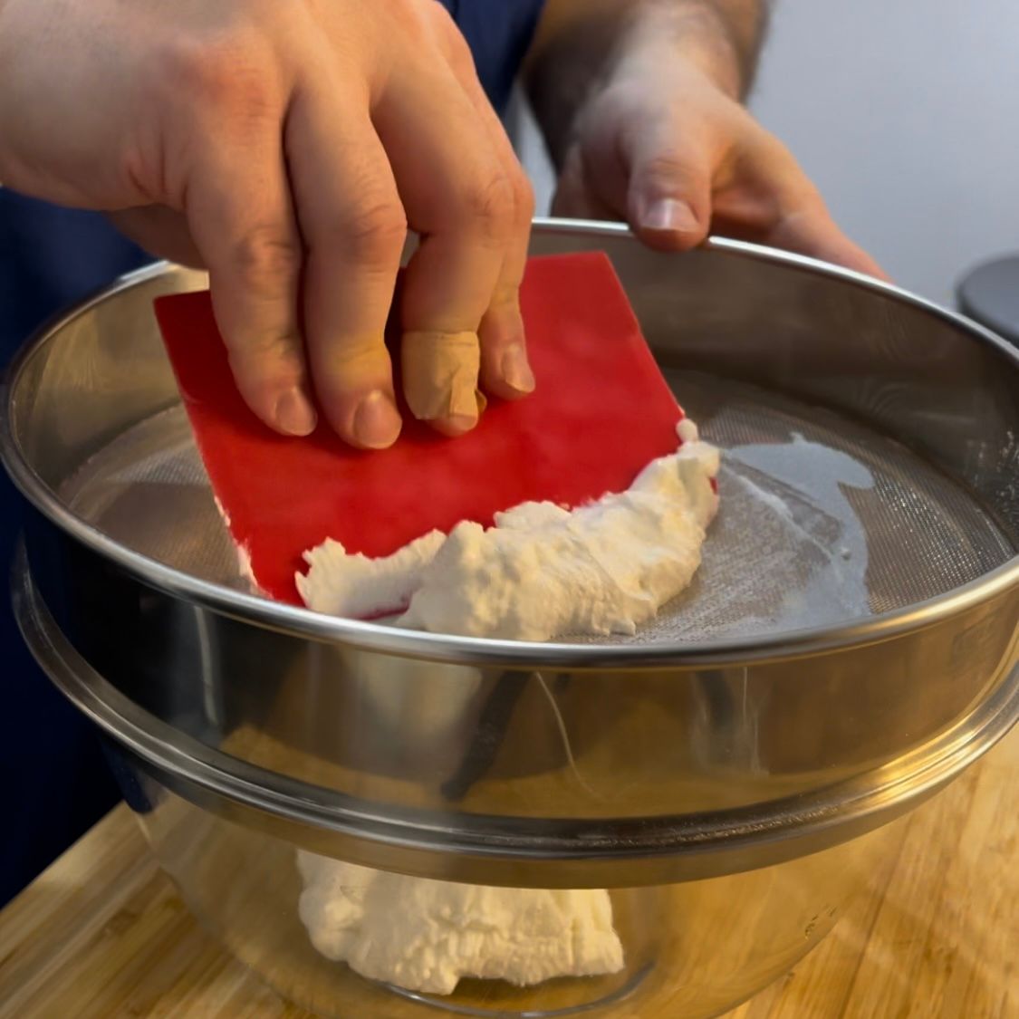 Una persona sta setacciando la ricotta con una spatola rossa