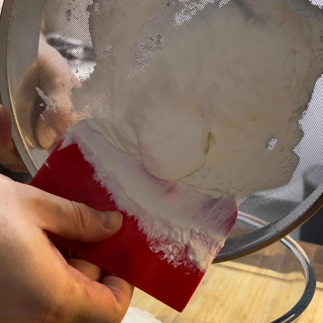 Una persona tiene una spatola rossa davanti a un setaccio con la ricotta