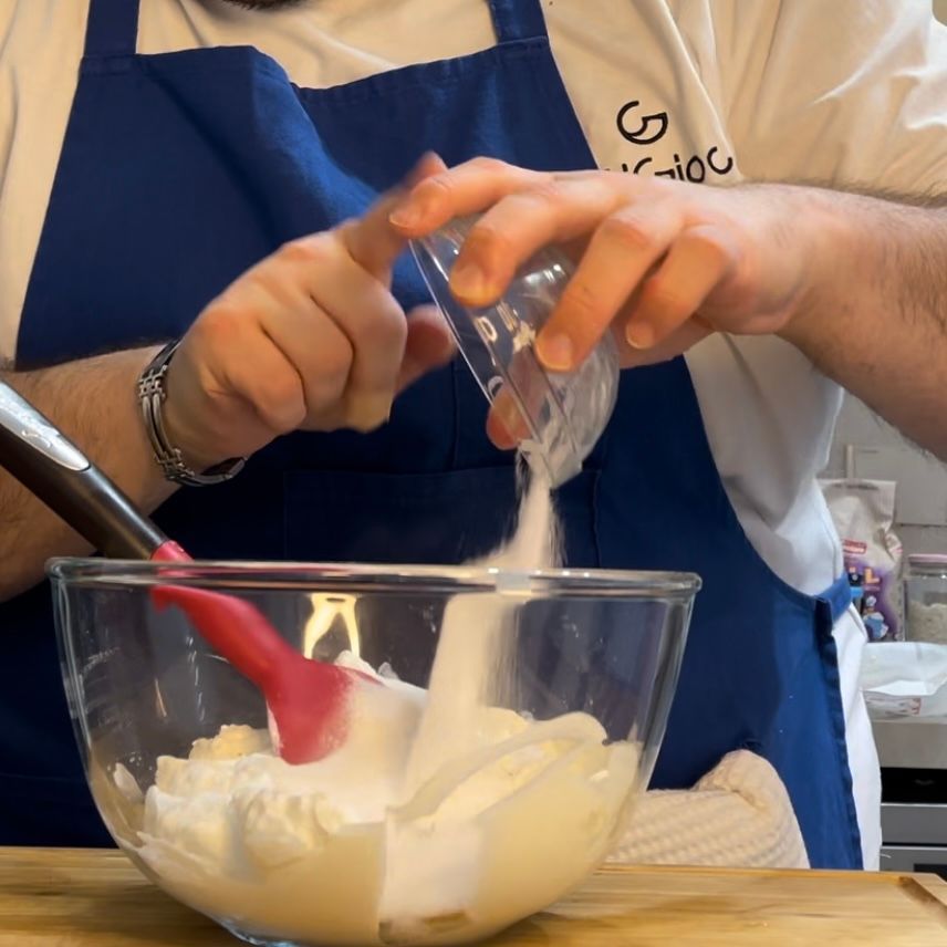 Una persona che versa lo zucchero in una ciotola di vetro e la ricotta 