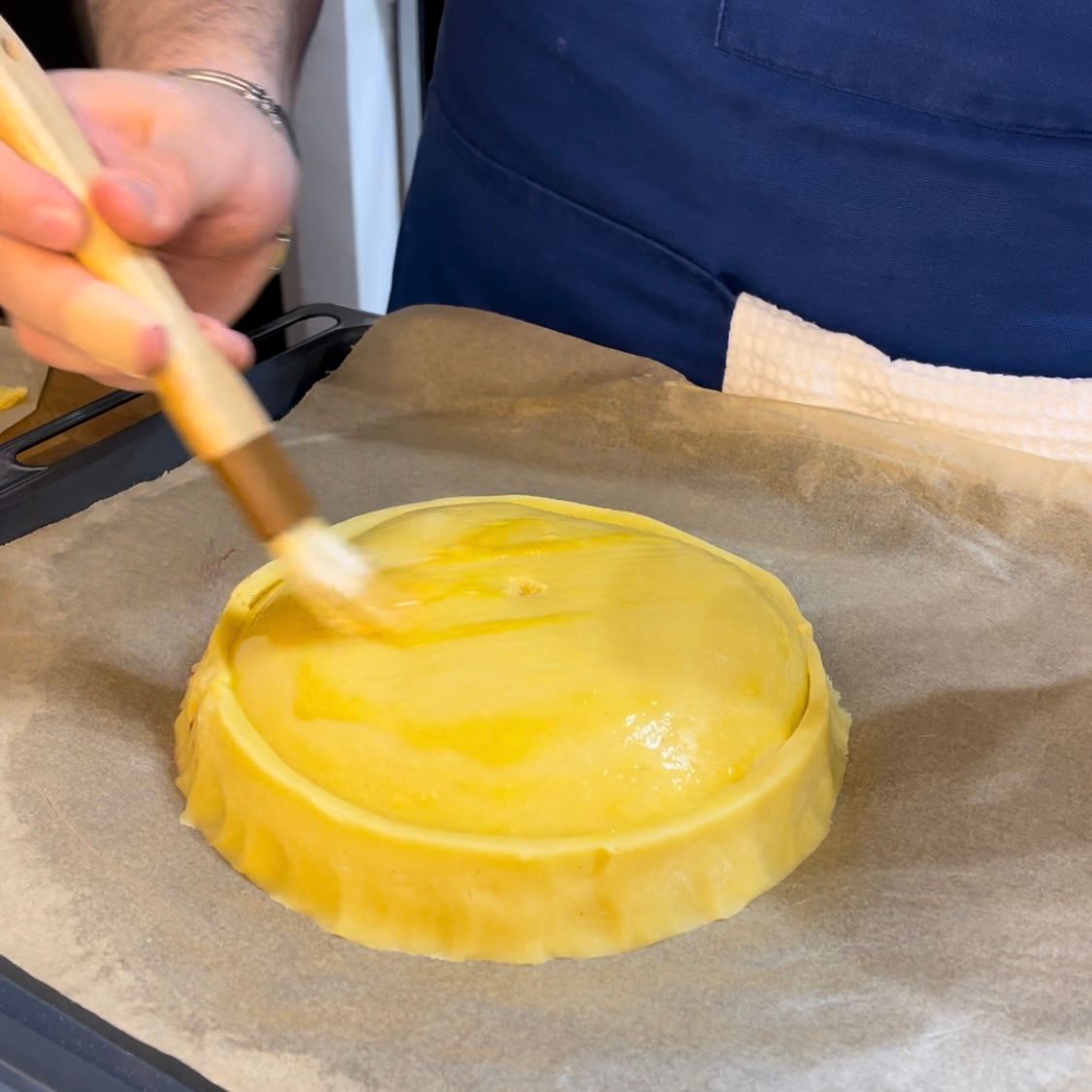 Una persona sta usando un pennello per spennellare l'uovo su una crostata ricotta e visciole 