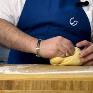 Un uomo con un grembiule blu sta impastando la pasta