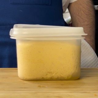 Un contenitore di plastica pieno di polvere gialla è appoggiato su un tavolo di legno.