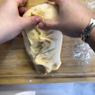 Una persona tiene in mano un pezzo di pasta su un tagliere di legno.