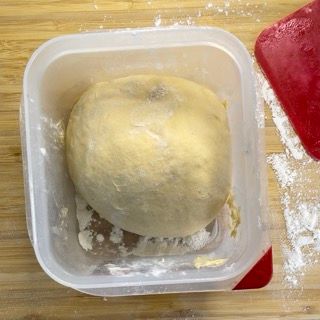 Una palla di pasta è in un contenitore di plastica su un tavolo di legno.
