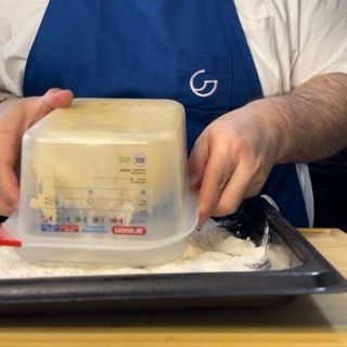 Una persona con un grembiule blu sta misurando il burro in un contenitore di plastica