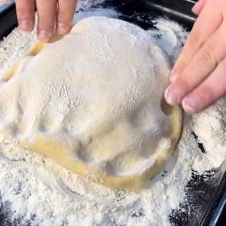 Una persona sta ricoprendo un pezzo di pasta con la farina