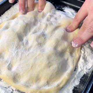 Una persona tiene in mano un pezzo di impasto in una padella ricoperta di farina.