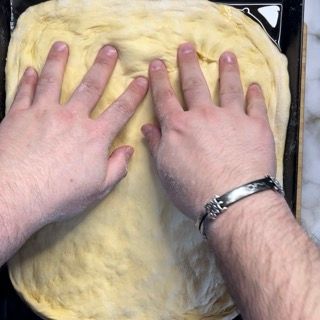 Una persona che indossa un braccialetto sta toccando un impasto per pizza
