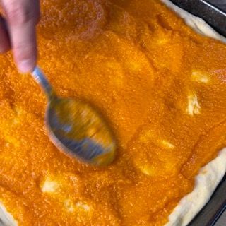 Una persona sta spalmando la salsa su una pizza con un cucchiaio.