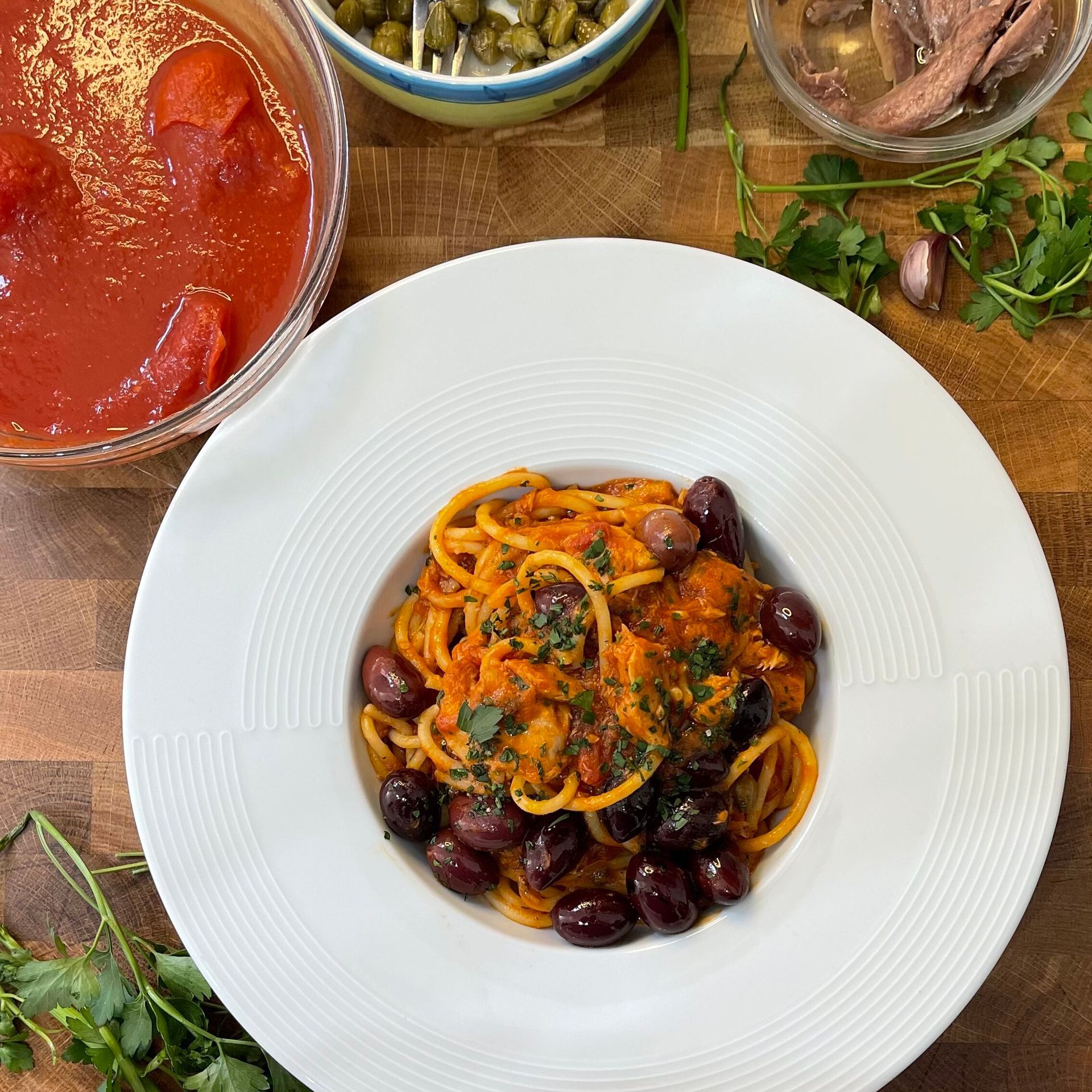 Un piatto bianco con sopra spaghetti e olive su un tavolo di legno.