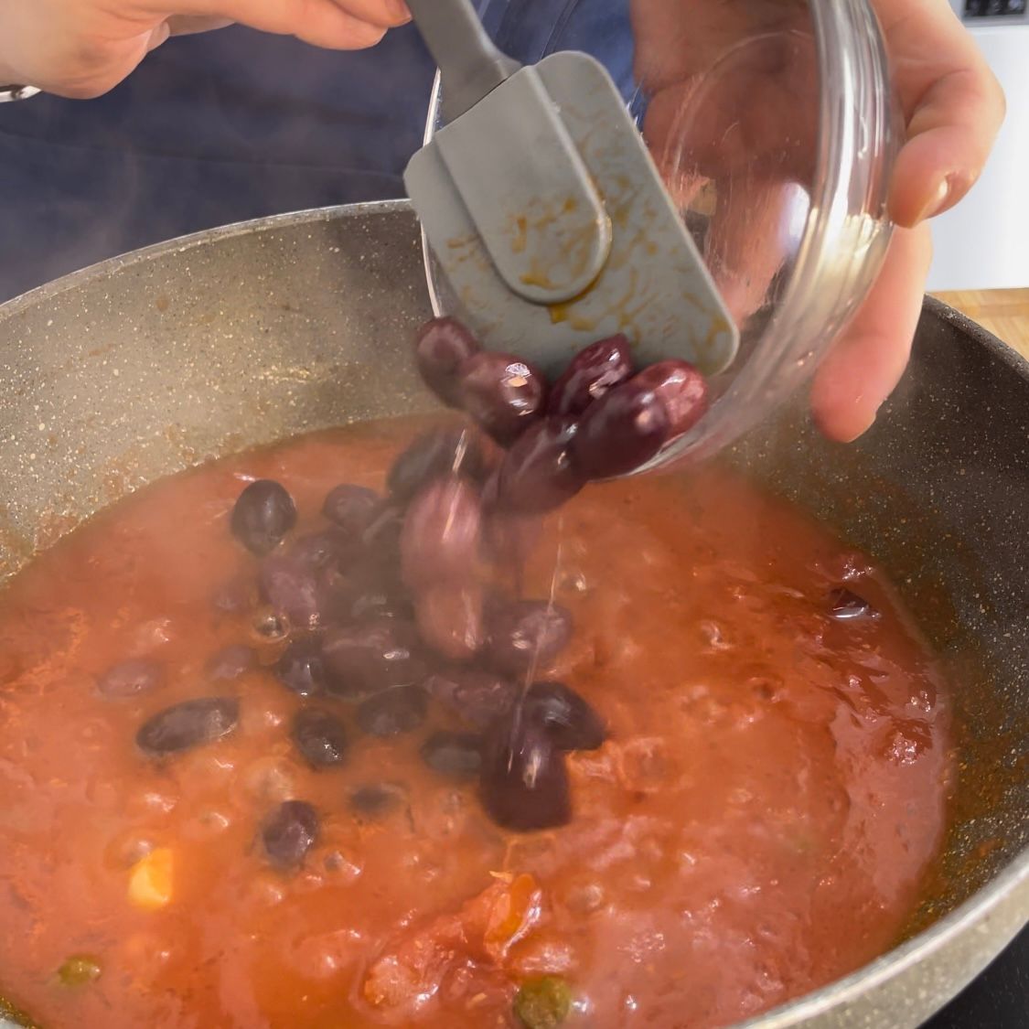 Una persona sta versando le olive in una pentola di salsa
