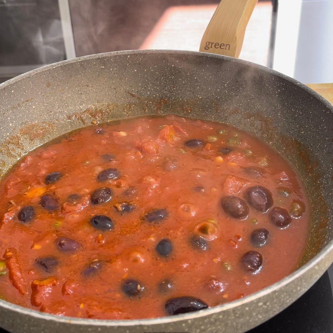 Una padella piena di salsa di pomodoro e olive con un manico verde