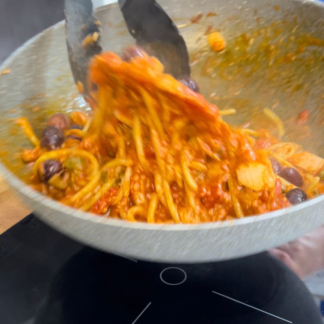 Una padella piena di spaghetti e olive viene mescolata con le pinze